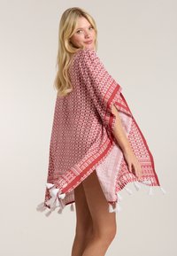 Sarkans un balts ar rakstu pončo ar pušķiem, ar brīvu piegriezumu un atvērtām malām, kas nodrošina ērtu valkāšanu. Viegls audums ar ģeometrisku dizainu.