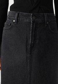 Black denim skirt with a high waist, featuring front pockets, a button closure, and subtle stitching detail. Smooth texture.