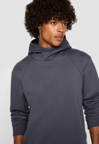 Felpa grigia con cappuccio caratterizzata da un collo alto, maniche raglan, tessuto morbido e polsini a costine, progettata per comfort e calore.