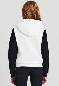 Felpa con cappuccio di colore bianco con maniche nere. Tessuto morbido, polsini e orlo a coste. Presenta una tasca a marsupio e una vestibilità rilassata.