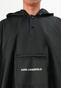 Zwarte hoodie-jack met een ritszak aan de voorkant en het witte "KARL LAGERFELD" logo op de zak, gedragen door een persoon.