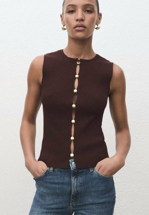 Top senza maniche a righe marrone con chiusura a bottoni frontale in metallo dorato e vestibilità aderente. Abbinato a jeans in denim azzurro.