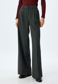 Brede broekspijpen in donkergrijze stof, met een hoge taille, plooien aan de voorkant en een zijringdetail voor extra accent.