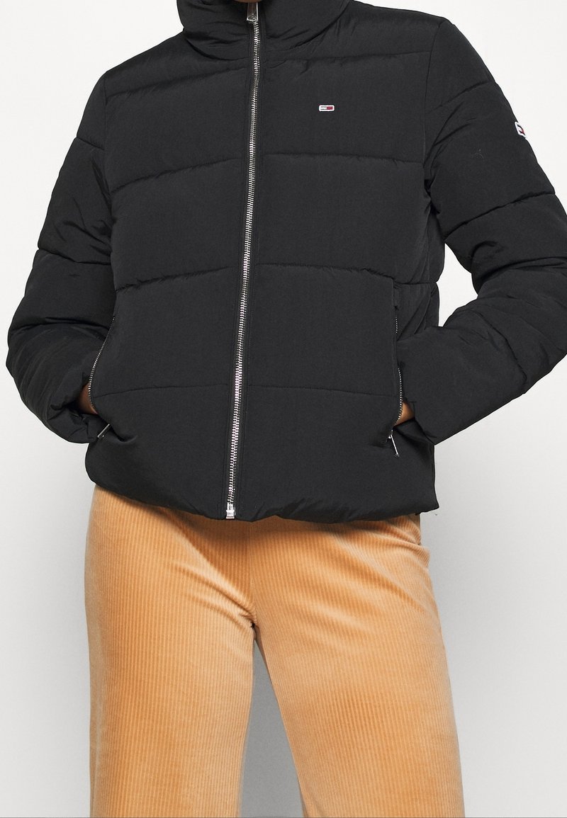 Czarna kurtka puchowa z wysokim kołnierzem, zapinana na zamek, z elastycznymi mankietami. Posiada pikowany wzór oraz niewielki detal z logo na klatce piersiowej.