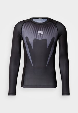 Długi rękaw koszulki sportowej w czerni i szarości, z teksturowanym wzorem, wyraźnym logo na klatce piersiowej oraz gładkim materiałem.