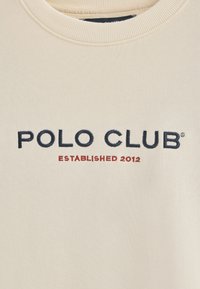 Sudadera color crema con textura acanalada que presenta el bordado "POLO CLUB" en azul marino y "ESTABLECIDO 2012" en rojo debajo.