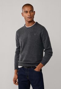 Donkergrijze gebreide trui met een ronde hals, geribbelde mouwen en onderrand. Gedragen over een wit shirt, in combinatie met donkere spijkerbroeken.