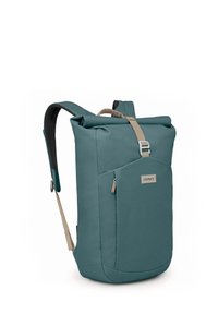 Mochila de color azul verdoso con correas beige. Fabricada en tejido texturizado, cuenta con un bolsillo frontal y el logo de Osprey. Cierre ajustable en la parte superior.