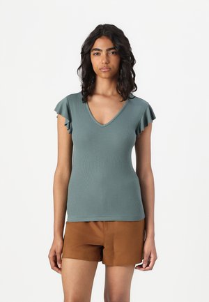 Kurzärmliges Oberteil in Teal mit V-Ausschnitt und Rüschendetails an den Schultern, aus geripptem Stoff; kombiniert mit braunen Shorts.