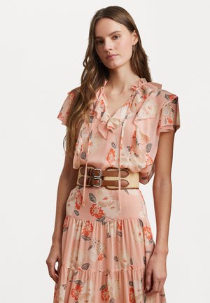 Blouse florale rose avec encolure à volants, manches courtes et taille ajustée, assortie d'une large ceinture beige avec deux boucles en argent.