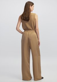 Top senza maniche color beige con texture a coste abbinato a pantaloni larghi color beige a superficie liscia. Vita elastica con una sottile lucentezza.