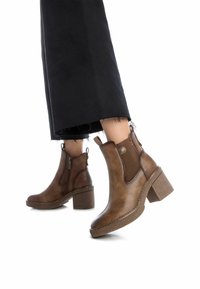 Botas de tobillo de cuero marrón con un tacón bloque texturizado y cremalleras laterales. Presenta paneles elásticos y detalles de costura en contraste.