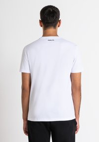 Camiseta de algodón blanca con mangas cortas, escote redondo y logo negro "MORATO" en la parte trasera. Textura suave con un corte relajado.