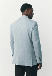 Lyseblå blazer lavet af tekstureret stof, med en klassisk pasform, indsnit ved kraven og fire sorte knapdetaljer på hver ærme.