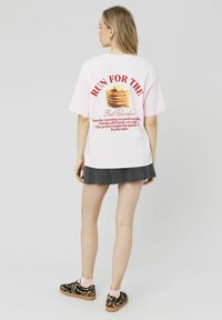 T-shirt en coton rose avec le texte "COURIR POUR LES MEILLEURES CRÊPES" et un graphique de crêpes dans le dos. Associé à une jupe plissée noire et des chaussures à imprimé léopard.