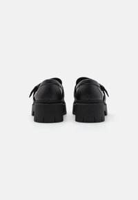 Chaussures en cuir noir avec une semelle épaisse, présentant une texture lisse et un détail décoratif de lacet à l'arrière.