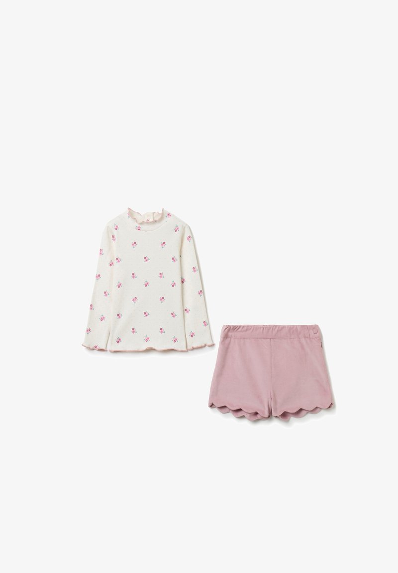 Langärmliges Oberteil in Creme mit pinkem Blumenmuster und Rüschensaum; kombiniert mit pinken Shorts mit gewelltem Saum. Glatte Textur, lässiges Design.