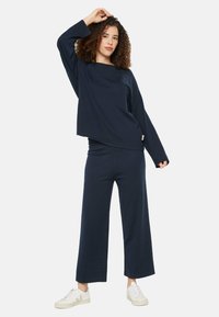 Dunkelblaues Zweiteiler-Outfit mit einer lockeren Bluse mit langen Ärmeln und weitem Hosenbein, aus weichem Stoff, kombiniert mit weißen Sneakern.