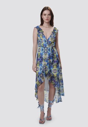 Blumiges Wickelkleid aus blauem, grünem und gelbem Chiffon, mit tiefem V-Ausschnitt, Rüschensleeves und asymmetrischem Saum. Abgerundet mit geschnürten Sandalen.
