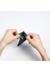 Poche noire refermable en cours d'ouverture par deux mains, avec un intérieur lisse et brillant et un extérieur mat affichant du texte et des graphiques.