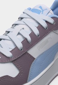 Κοντινό πλάνο αθλητικού παπουτσιού Puma με λευκά κορδόνια, ανοιχτό μπλε και μωβ δερμάτινα πάνελ, και λογότυπο Puma στο πλάι και στη γλώσσα του παπουτσιού.