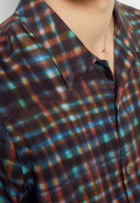 Camicia a maniche corte con un motivo a quadri multicolore caratterizzato da tonalità scure, che crea un effetto vivace con una texture di tessuto liscia e colletto a punta.