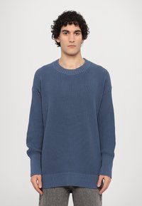Maglione lavorato a maglia di colore blu ardesia, con scollatura e polsini a coste, vestibilità ampia, tessuto strutturato e silhouette rilassata.