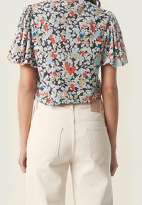 Blommig topp med korta puffärmar i svart, röd, blå och beige; matchad med vita, högmidjade jeans med bakfickor och lätt texturerad tyg.