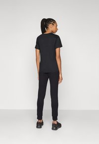 Zwarte katoenen t-shirt met korte mouwen, gecombineerd met zwarte taps toelopende joggers. De outfit heeft een casual, ontspannen pasvorm.