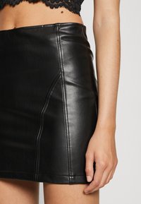 Minifalda de cuero negro con costuras visibles y detalle en la costura lateral. Textura suave con un diseño ajustado, que termina por encima de la rodilla.