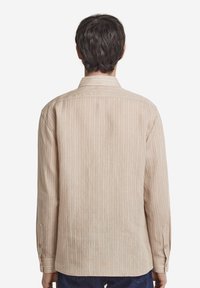 Camicia beige a maniche lunghe con righe verticali, polsini con bottoni e colletto. Realizzata in tessuto leggero con una finitura strutturata.