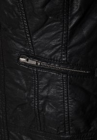 Svart läderjacka med texturerad yta, diagonal dragkedjeficka och sydda detaljer längs sömmarna.