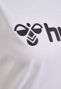 Hvid bomulds T-shirt med et sort grafisk logo med abstrakte designs og tekst, trykt fremtrædende på brystet.