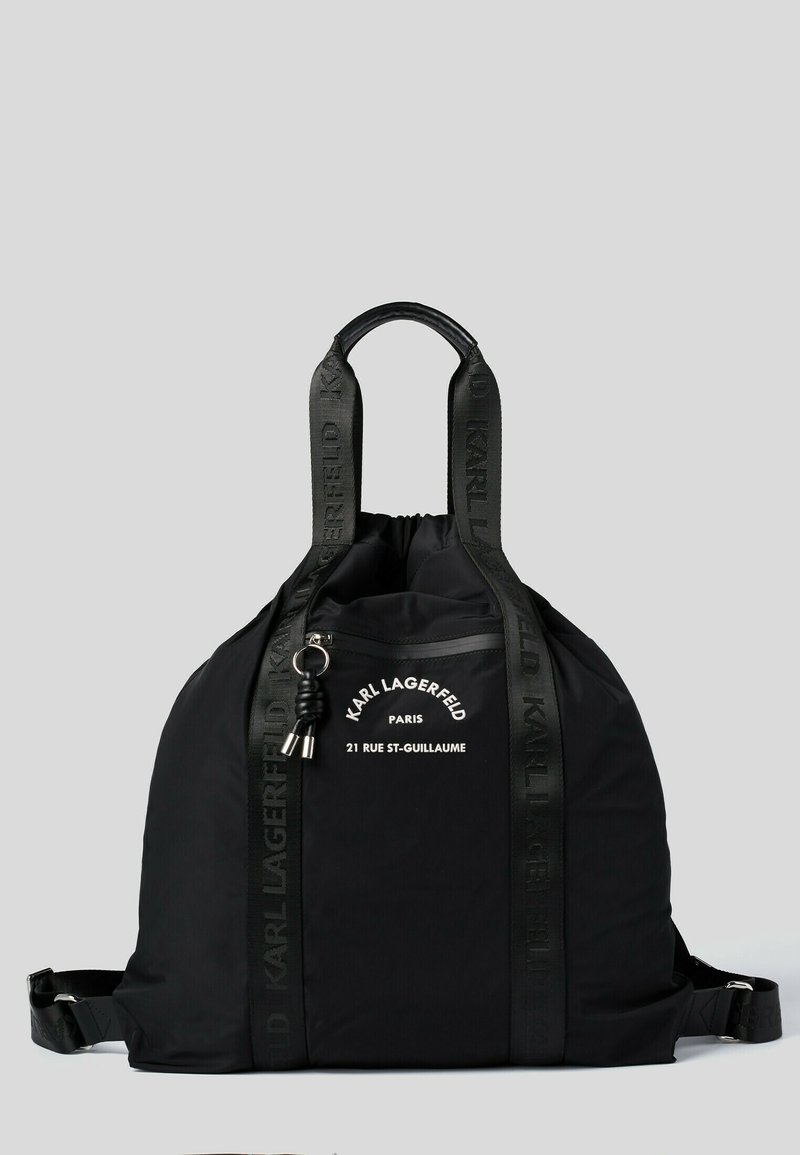 Sac à dos noir en nylon lisse avec deux poignées, des bretelles ajustables et une poche zippée à l'avant. Présente un logo et du texte en blanc.