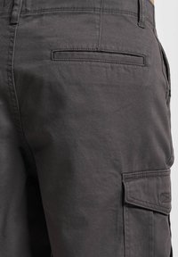 Graue Cargo-Hosen mit glatter Textur, seitlichen Taschen, einer kleinen Gesäßtasche und verstärkten Nähdetails.