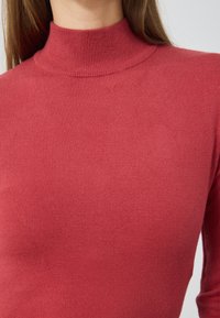 Czerwony sweter z wysokim kołnierzem, wykonany z dzianiny o prążkowanej fakturze. Dopasowany krój z miękkiego materiału, z długimi rękawami i bez widocznych wzorów.