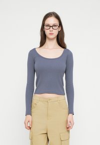 Top cu mâneci lungi, scurt, din țesătură nervurată albastru închis, cu un decolteu larg. Asortat cu pantaloni cargo kaki, cu buzunare laterale.