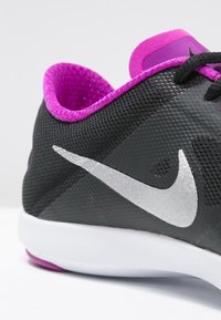Sneaker Nike neri e rosa con un prominente swoosh argento, che mostra un tessuto testurizzato e una suola bianca, posizionato su uno sfondo neutro.