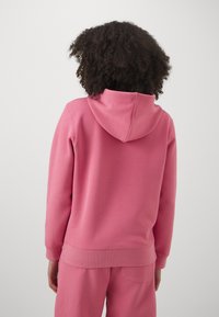 Felpa rosa realizzata in morbido tessuto con una vestibilità comoda, dotata di cappuccio con coulisse, polsini e orlo a coste, abbinata a pantaloni coordinati.