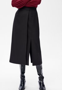 Zwarte midi-rok met een voorzijde split, gemaakt van gladde stof. Voorzien van een gestructureerde tailleband en valt tot halverwege de kuit, gecombineerd met zwarte kniehoge laarzen.