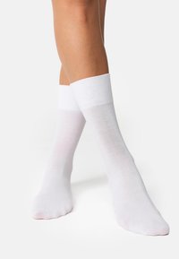Chaussettes en coton blanches avec un bord côtelé, design à hauteur de cheville et texture lisse. Dotées d'un orteil sans coutures pour plus de confort.