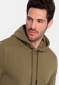 Sudadera verde oliva hecha de tela suave, con capucha ajustable, puños acanalados y un diseño limpio con un corte relajado.