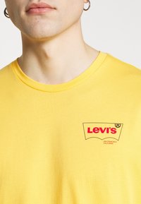 T-shirt di cotone giallo con logo rosso Levi's nella parte sinistra del petto. Collo rotondo e maniche corte. Tessuto liscio.