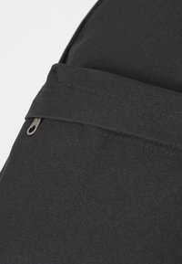 Sac en tissu noir avec une surface texturée. Présente une poche zippée à l'avant et une forme lisse et arrondie. Design minimaliste.