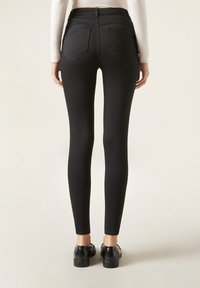 Vaqueros negros ajustados con una textura suave, cintura alta y dos bolsillos traseros. Combinados con zapatos negros, mostrando una silueta ajustada.