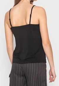 Černý bezramenný top s nastavitelnými ramínky, vyrobený z měkké látky, s volným střihem a hladkým povrchem, v kombinaci s pruhovanými kalhotami.