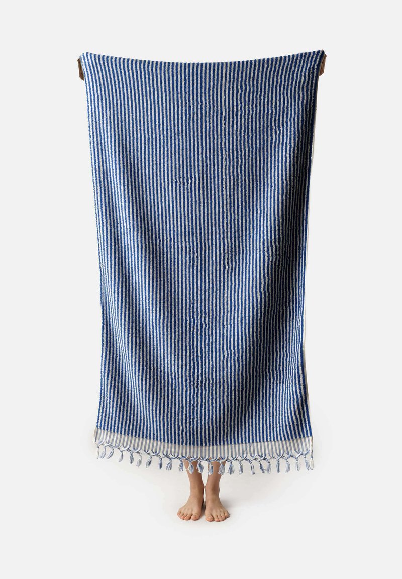 Manta de algodón a rayas azul y blanca con bordes con flecos, forma rectangular, superficie texturizada y borlas en la parte inferior.
