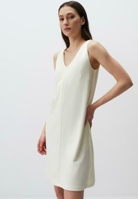 Abito bianco senza maniche con scollatura a V, dalla texture liscia e un dettaglio di tasca discreto sul lato, che offre un design minimalista.