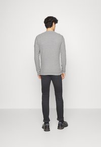 Szara, długosleeve'owa koszula z okrągłym dekoltem, zestawiona z ciemnymi dżinsami i czarnymi butami. Materiał wydaje się miękki o gładkiej teksturze.