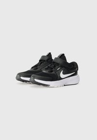 Schwarze Sportschuhe mit Mesh-Obermaterial, weißer Sohle, Riemen über den Schnürsenkeln und Nike-Swoosh-Logo. Verfügt über eine strukturierte Oberfläche und eine gepolsterte Sohle.